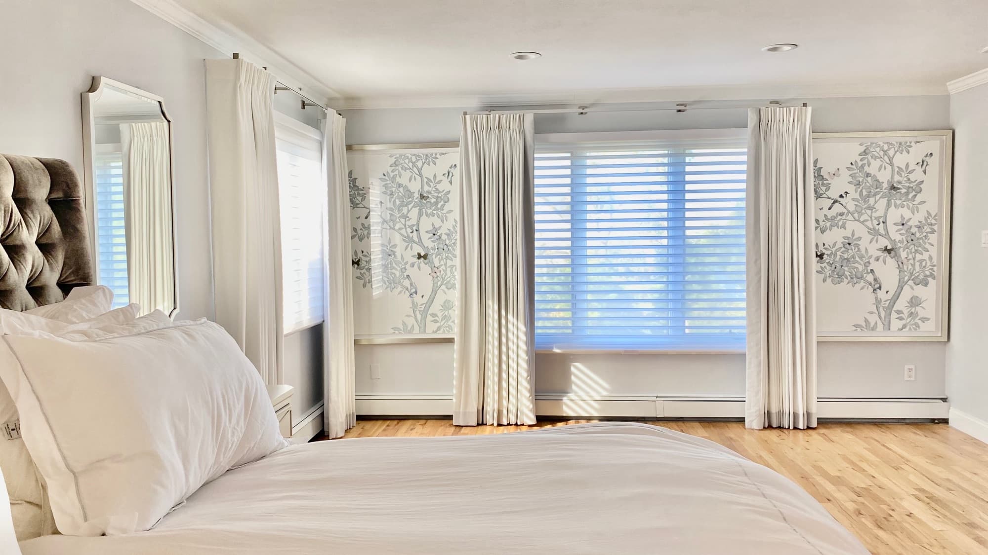 Custom pinch-pleat drapery and wood blinds in a bright Long Island primary bedroom